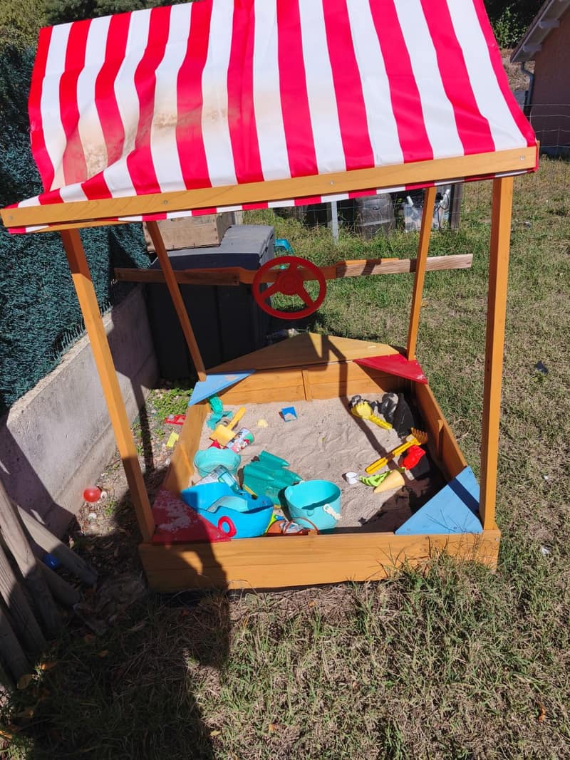 Bac à sable en bois avec toit rayé rouge et blanc, seaux, pelles et jouets de plage